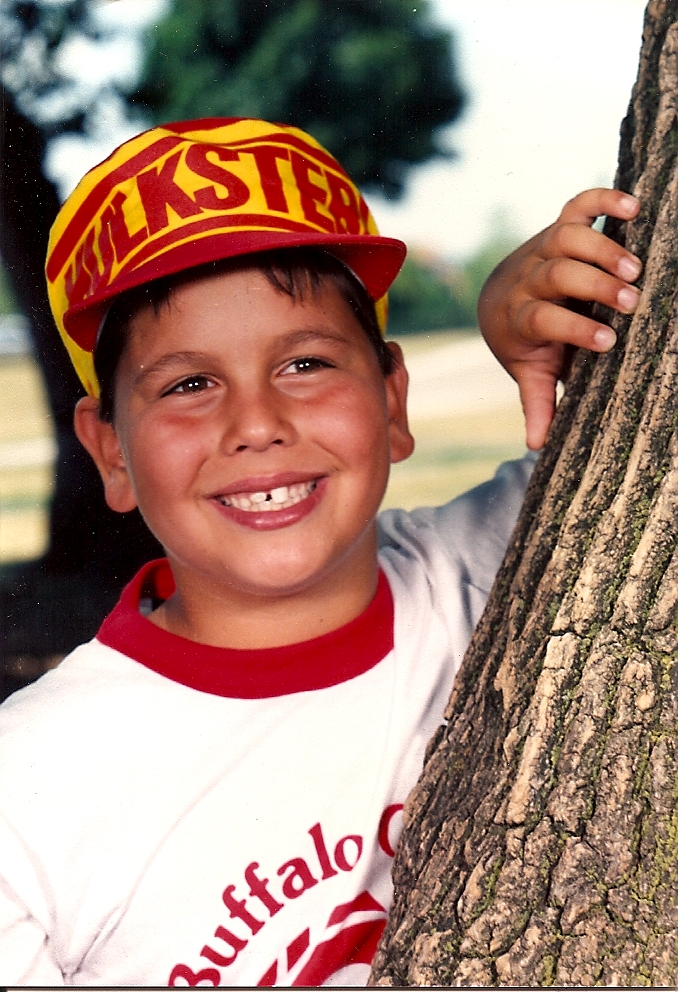 a boy smiling and leaning against a tree