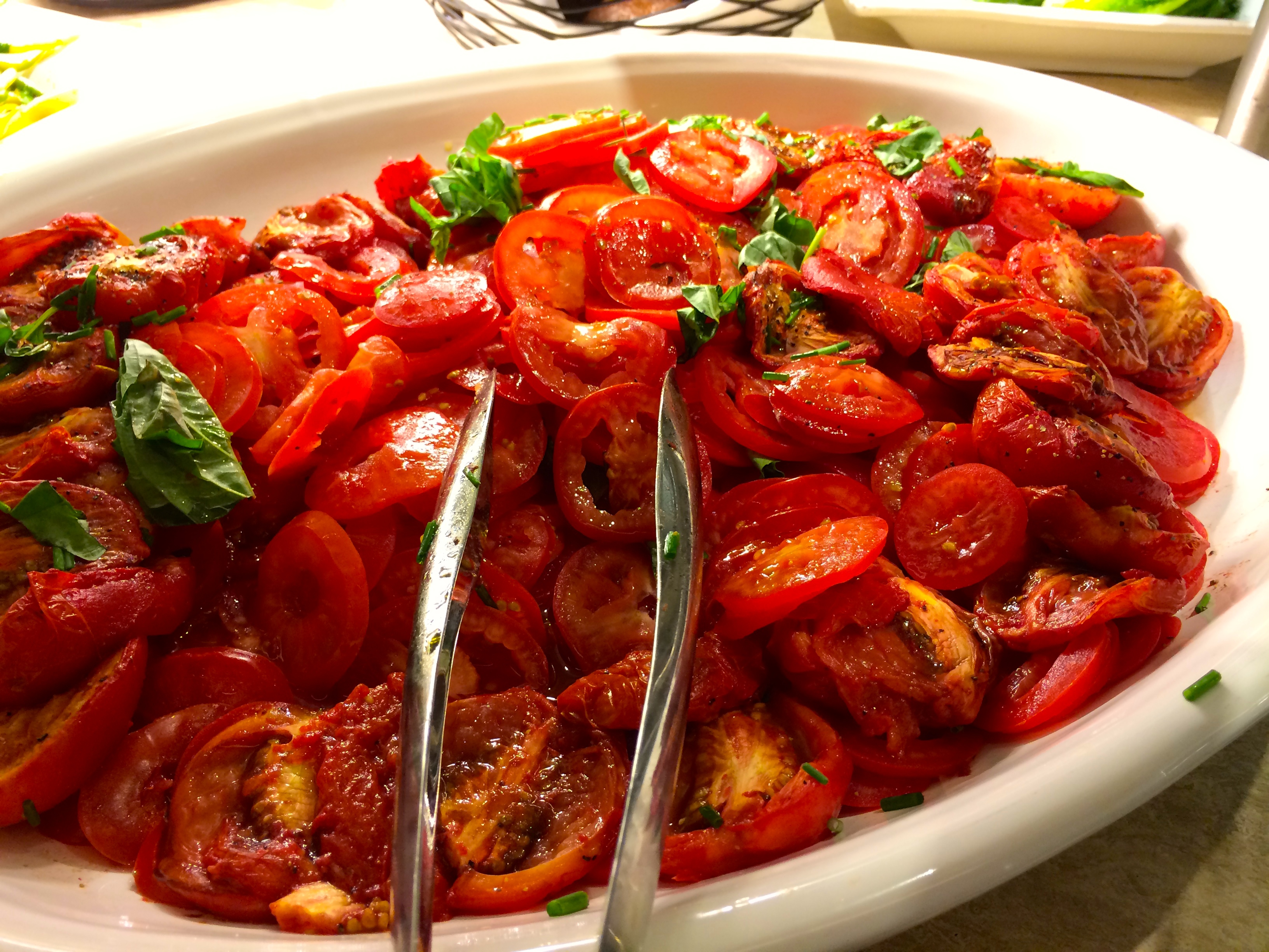 a bowl of tomatoes with tongs