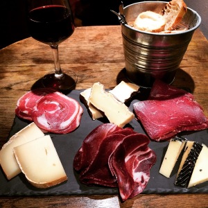 a plate of meat and cheese on a table with a glass of wine