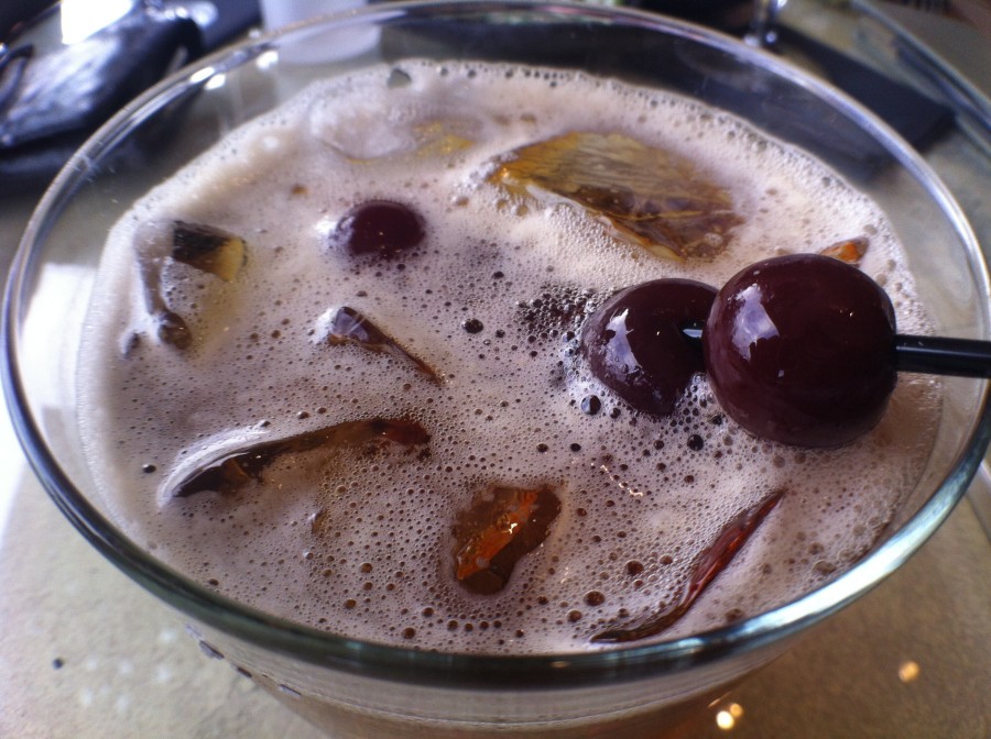 a glass with brown liquid and cherries
