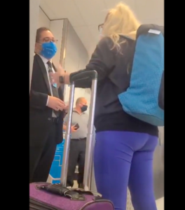 a woman wearing a blue backpack and purple pants with a blue backpack standing next to a man wearing a blue face mask