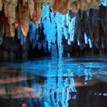a cave with water and stalactites with Reed Flute Cave in the background