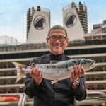 a man holding a fish in front of a cruise ship