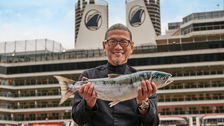 a man holding a fish in front of a cruise ship